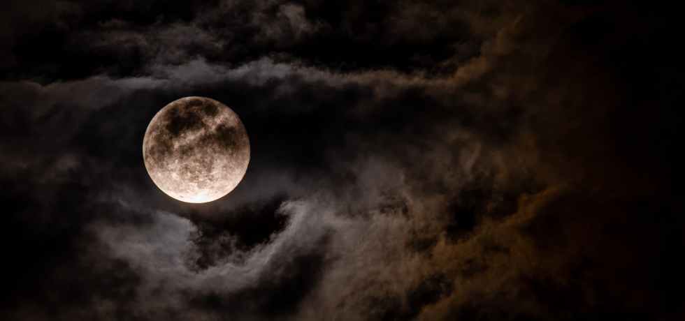 A spooky view of the moon behind moonlit clouds.