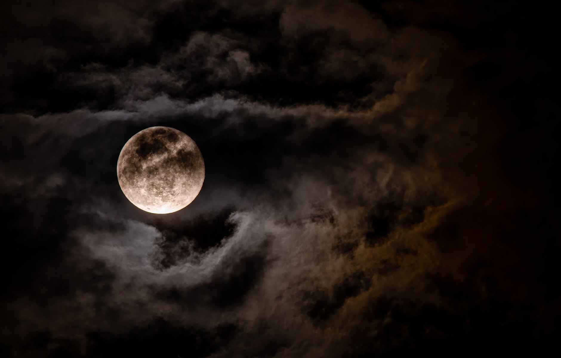 A spooky view of the moon behind moonlit clouds.